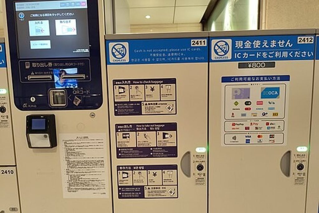 Station lockers at Osaka Station with a sign saying cash is not accepted and a touch-screen pay station for IC cards and other cashless payment