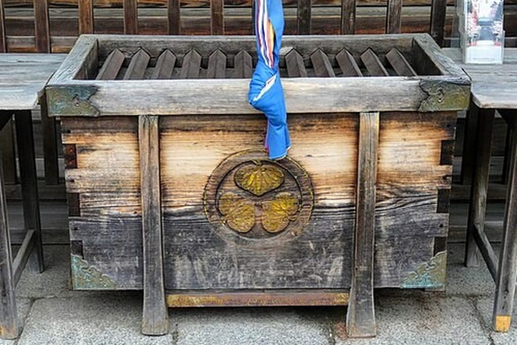 Weathered wooden offertory box with a slatted top and a hollyhock crest at Sendai Tosho-gu shrine