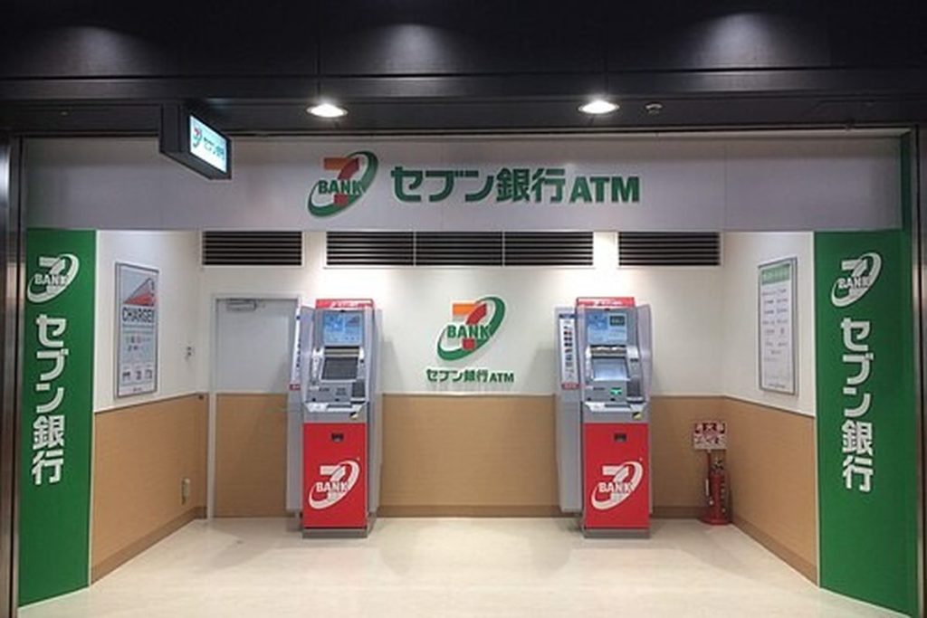 Seven Bank ATM corner with two red and white ATMs and green Seven Bank signs in the Dojima underground mall, Osaka