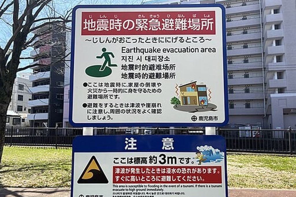Green and white sign marking an earthquake evacuation area in Japanese, English, Korean and Chinese, with a tsunami caution panel showing the ground is 3 metres above sea level