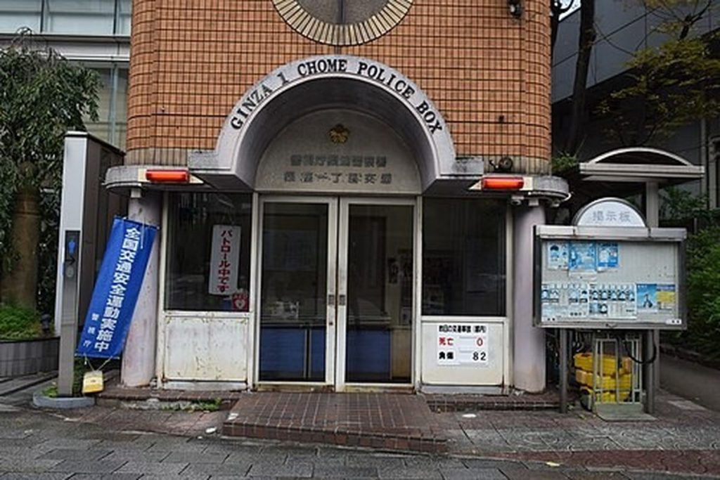 Small brick koban police box in Ginza, Tokyo, with a curved sign reading Ginza 1 Chome Police Box above the entrance and a red lamp