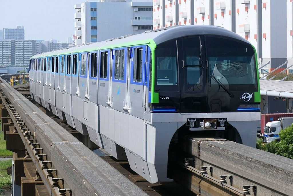 A white Tokyo Monorail train with blue and green stripes on its elevated concrete guideway