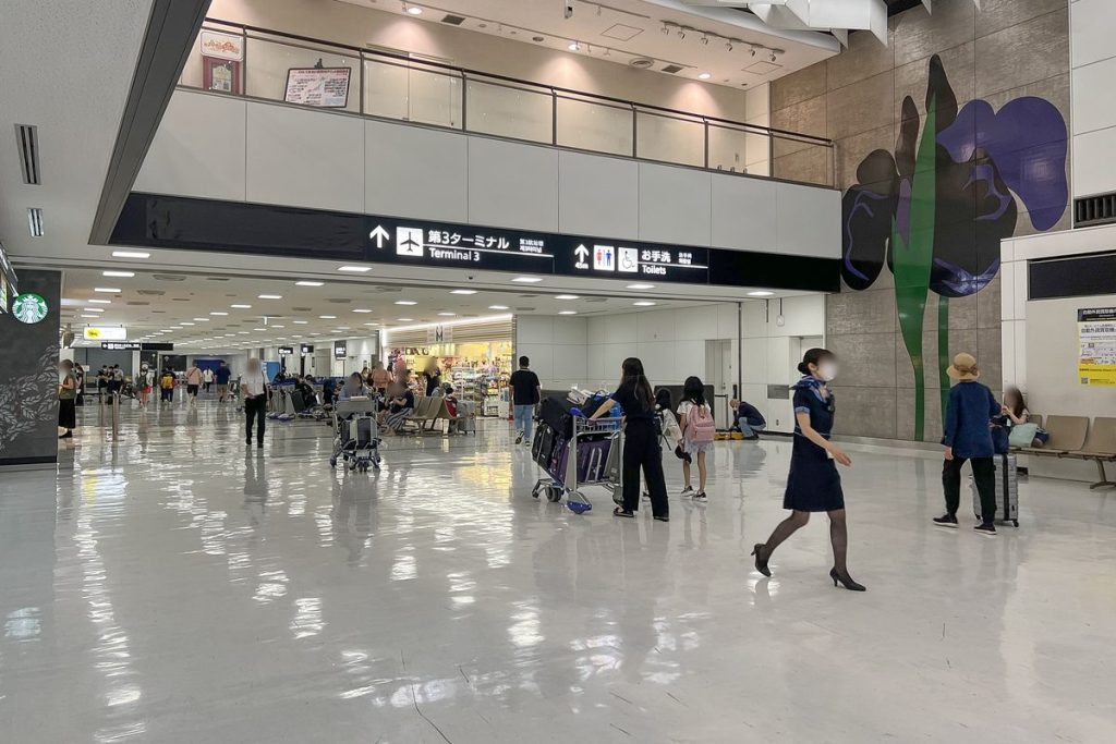 Bright north arrival hall at Narita Airport Terminal 2 with travelers pulling suitcases under overhead signs and a mezzanine