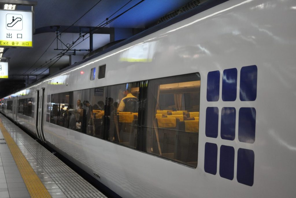 White JR Haruka limited express train with its window-grid design waiting at a platform in Kansai-airport Station, with an exit sign above the platform