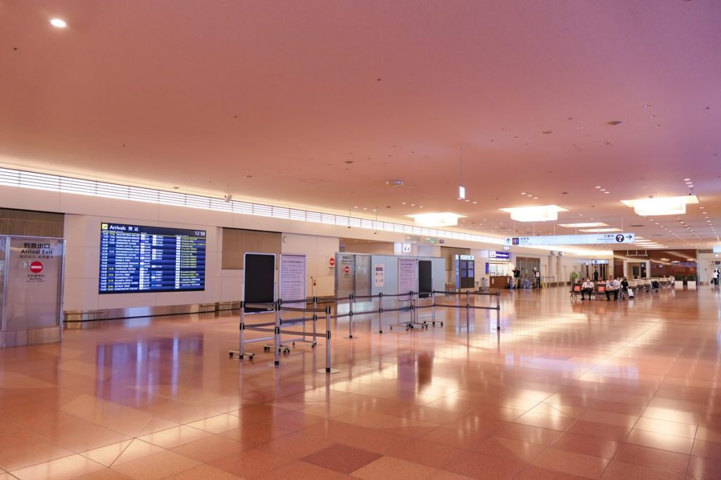 Wide, quiet arrival lobby of Haneda Airport Terminal 3 with a polished floor, an arrivals board and service counters along the wall