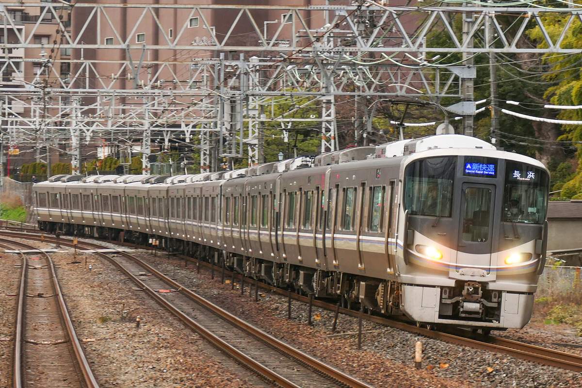 A silver JR West 225 series Special Rapid train with its headlights on, running on the JR Kyoto Line between Osaka and Kyoto