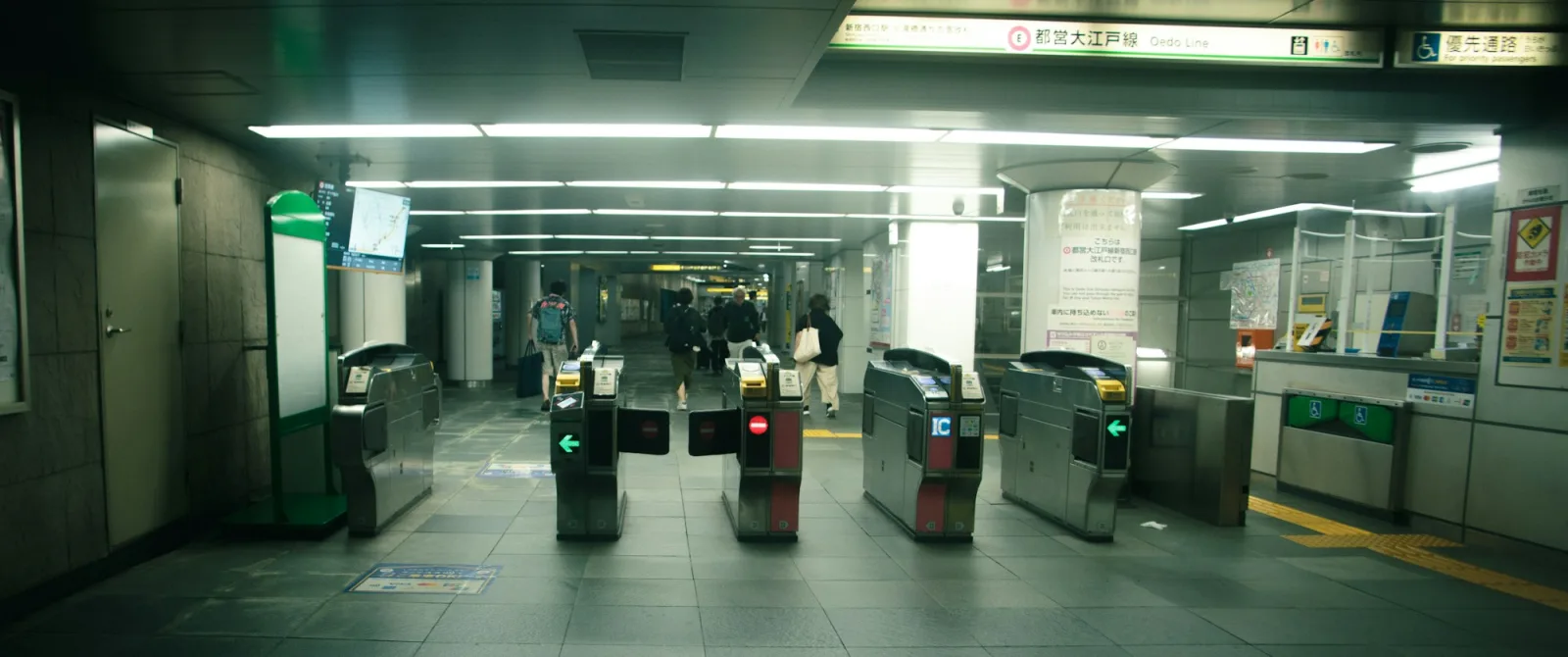 Ticket gates with IC-card readers at a Tokyo subway station in Shinjuku, with commuters walking away from the camera