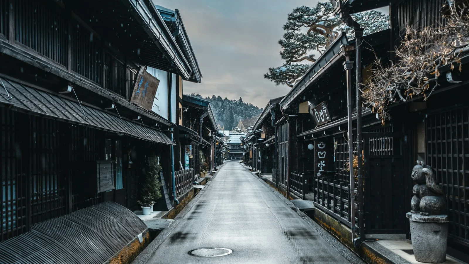 A quiet old-town street in Takayama with dark wooden lattice-fronted merchant houses, small water channels and light snow